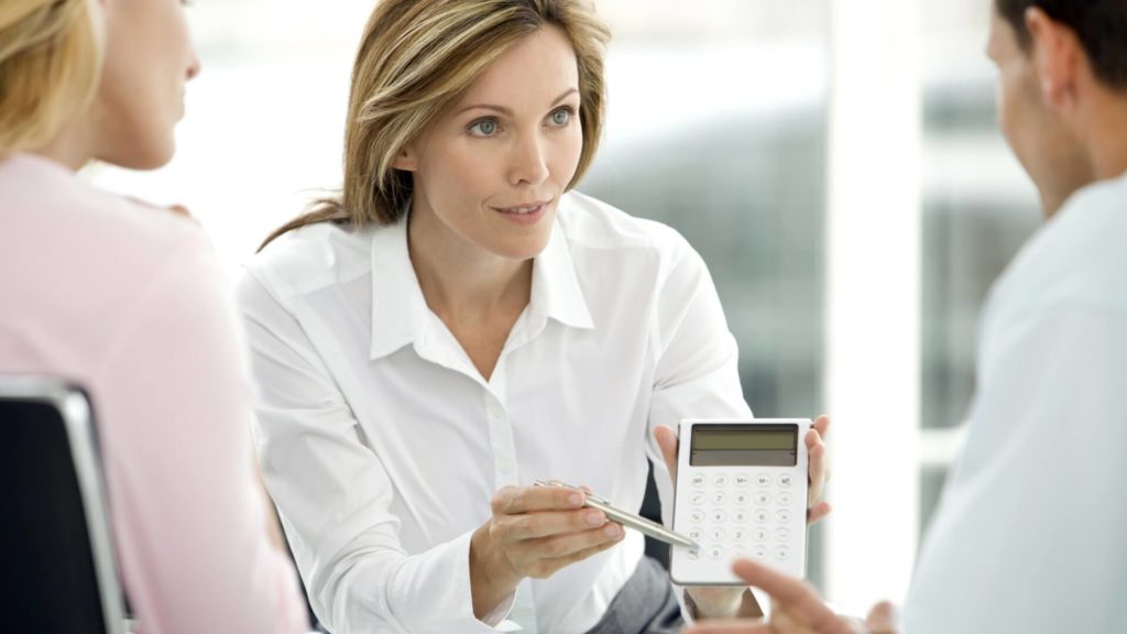 two people speak with a financial advisor, who is holding a calculator in front of them